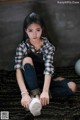 A young woman sitting on the floor wearing a plaid shirt and jeans.