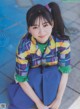 A young woman sitting on the ground wearing a colorful shirt and skirt.